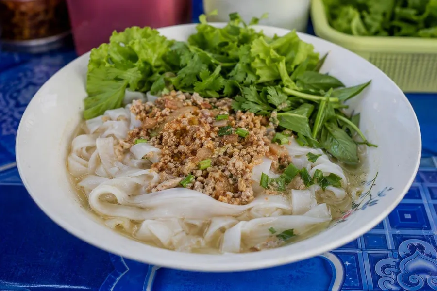 Khao soi op de avondmarkt van Luang Namtha combineert brede rijstnoedels, vleessaus en heldere bouillon.