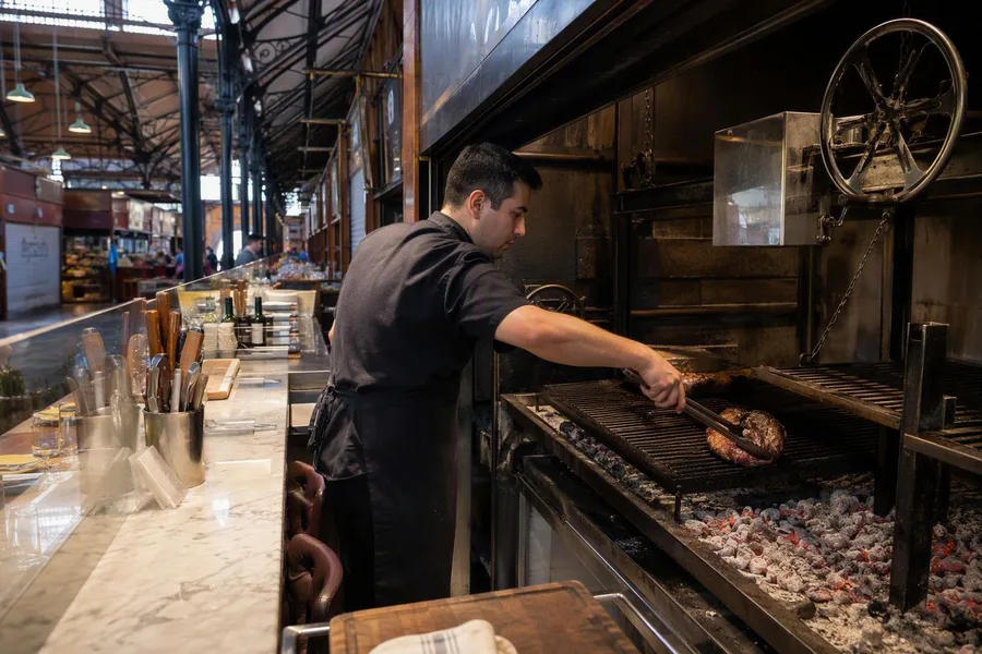 Bij Hierro Parrilla legt een kok een afgekoelde portie terug op de houtskoolgrill.