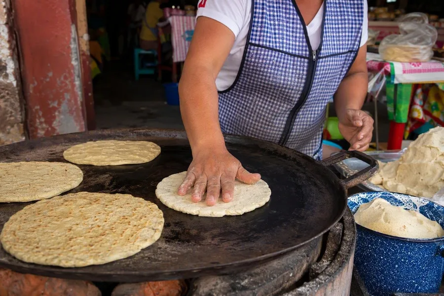 A vendor presses a thick memela from masa onto a hot comal at Mercado de la Merced.
