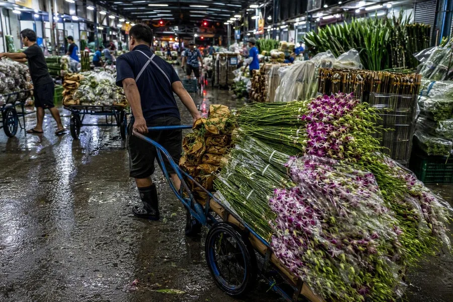 Werkers verplaatsen bloemenkarren en bundelen stelen in de overdekte markthallen van Pak Khlong Talat.