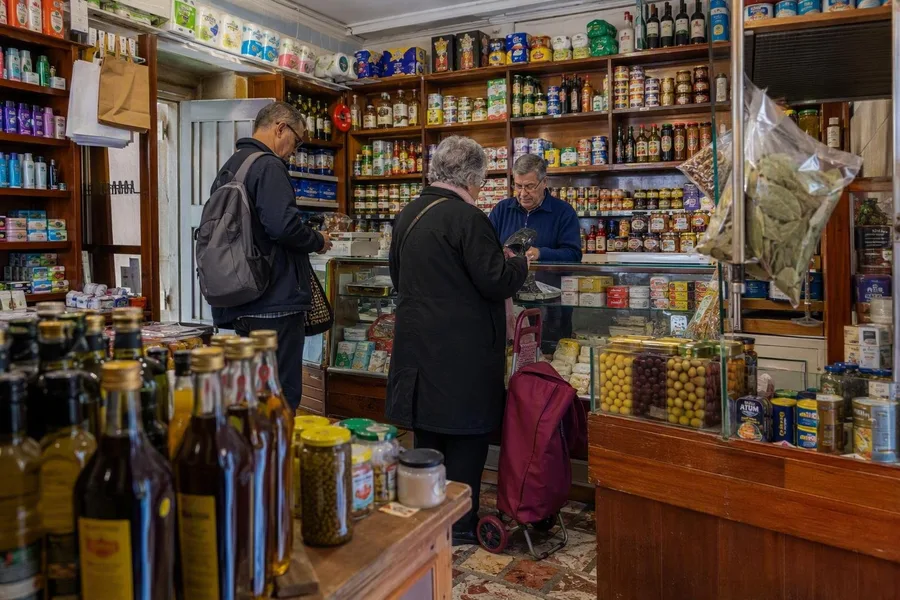 Klanten doen boodschappen bij Mercado Abastecedor de Alfama aan Travessa do Terreiro do Trigo.