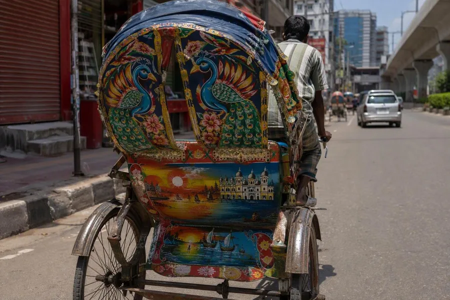 Een bestuurder trapt op een fietsriksja in Dhaka met een beschilderde blikken kettingkast.