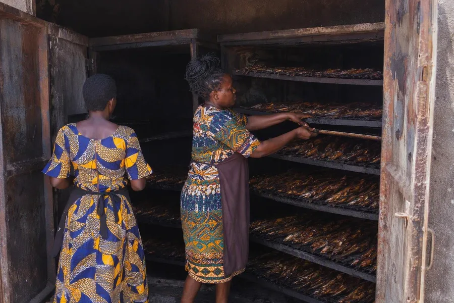 Vrouwen roken vis in een gesloten oven bij Kigungu Fish Landing Site.