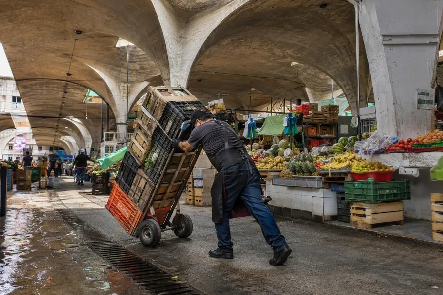 Een diablero duwt een geladen steekwagen langs groentekramen in de Nave Mayor van La Merced.