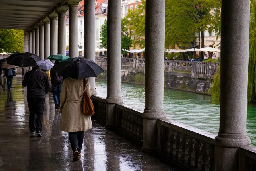 Voetgangers met paraplu's lopen onder de marktcolonnade langs de Ljubljanica.