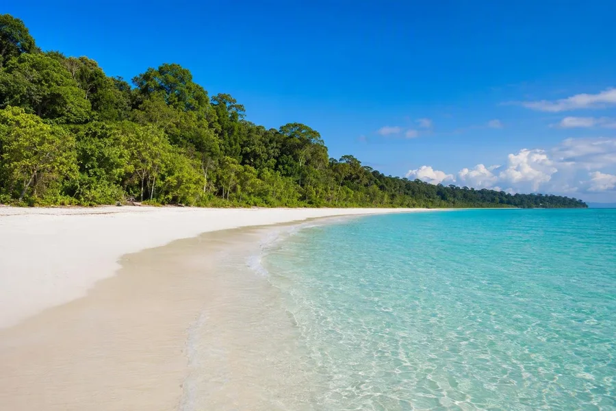 Dicht bos grenst aan het brede witte zand en turquoise zwemwater van Radhanagar op Swaraj Dweep.