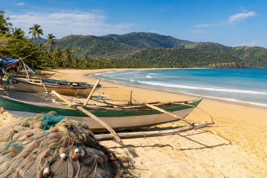 Vissersboten en netten liggen op Nacpan Beach, met palmen en beboste heuvels op Palawan.