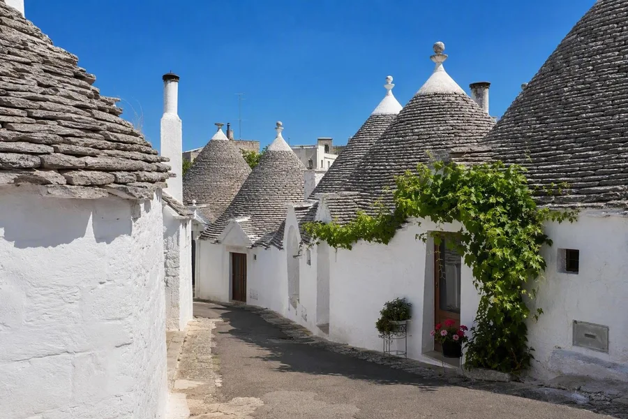 Witgekalkte trulli met gelaagde kegelvormige daken staan langs woonstraten in Aia Piccola in Alberobello.