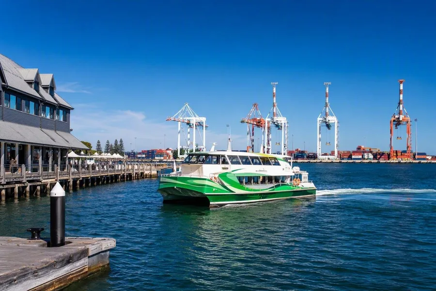 Een veerboot steekt het bassin bij Victoria Quay over, met containerkranen op North Quay erachter.