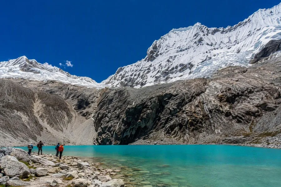 Wandelaars bereiken de stenige oever van Laguna 69 onder Chacraraju in Nationaal Park Huascarán.