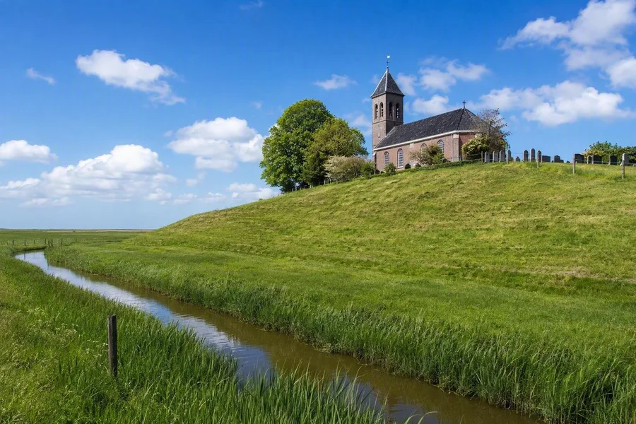 Kerk en kerkhof van Hegebeintum rijzen boven kleivelden en sloten uit.