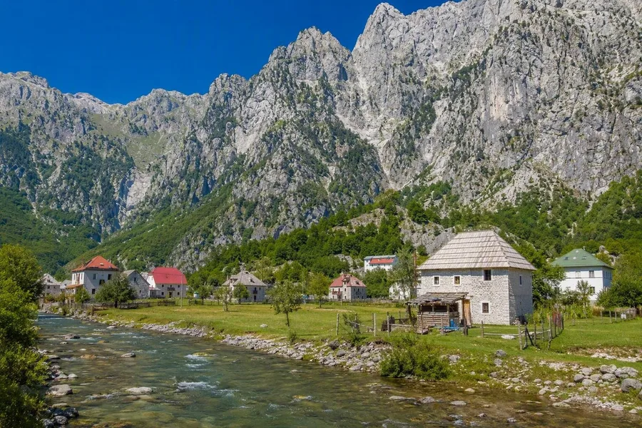 Stenen huizen staan bij de rivier onder kalksteenwanden in het gletsjerdal van Theth.