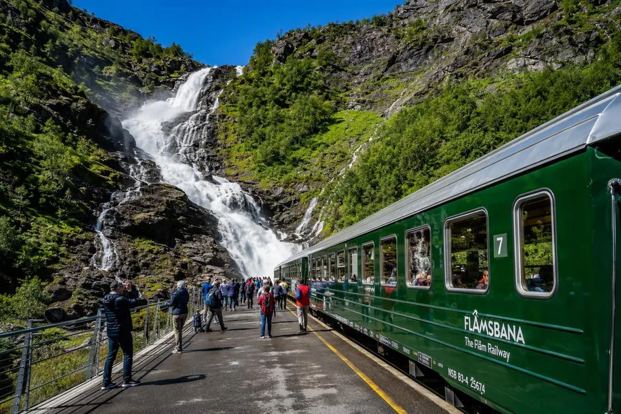 Passagiers staan bij de Kjosfossen-waterval tijdens een stop van de Flåmsbana.