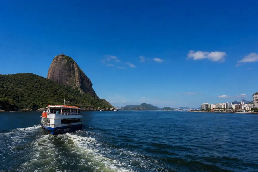Een boot vaart over Guanabara Bay, met Pão de Açúcar en Niterói in beeld.