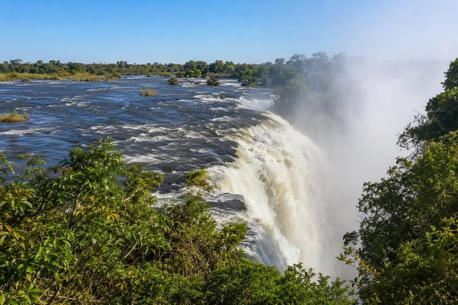 De Zambezi stort bij Victoria Falls over de basalt rand en stuurt nevel door het Zimbabwaanse bos.