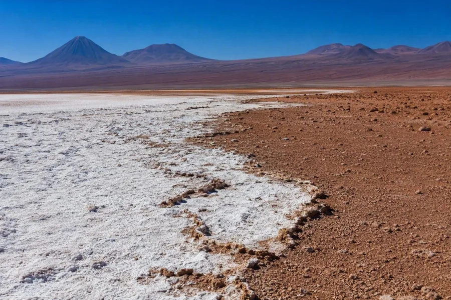 Witte zoutkorsten grenzen aan bruin-oranje vulkanische bodem in de Salar de Atacama in Chili.