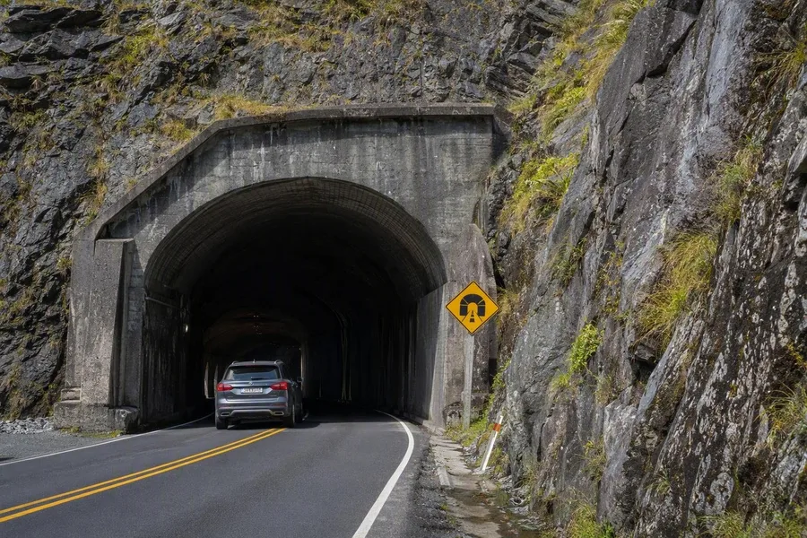 Een auto rijdt de granieten Homer Tunnel op Milford Road in Fiordland binnen.