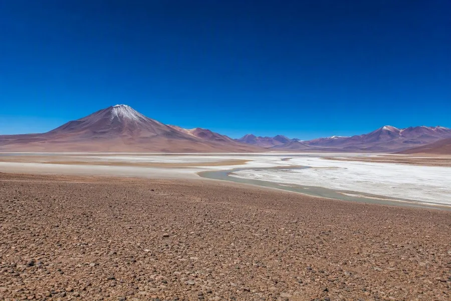 Een kale grindvlakte en zoutbekken strekken zich uit naar hoge Andesplateaus in de Atacama.