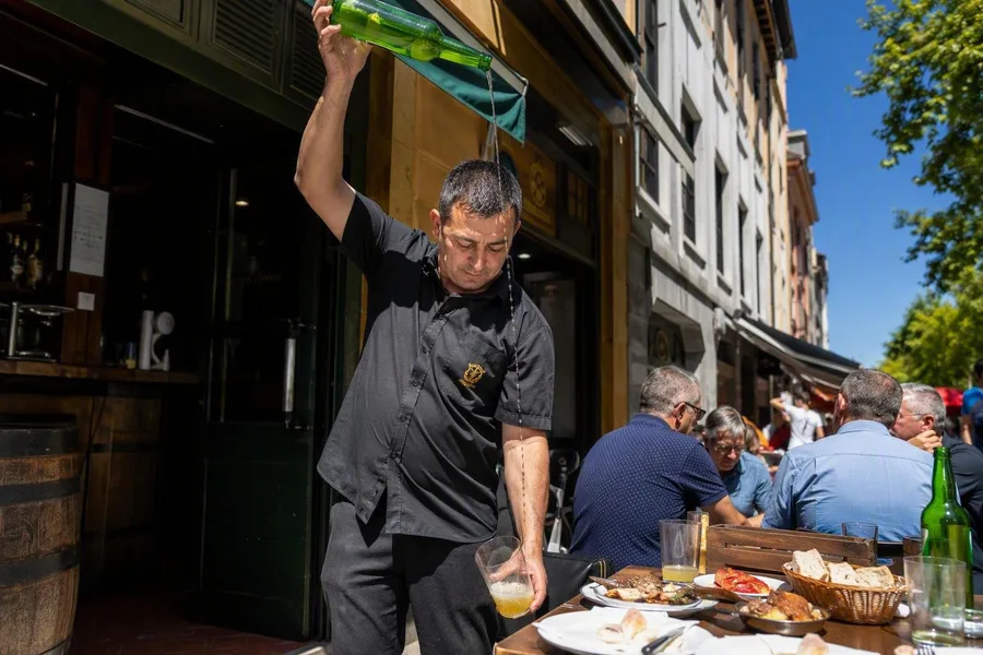 Een schenker giet cider van grote hoogte in een breed glas aan de Calle Gascona in Oviedo.