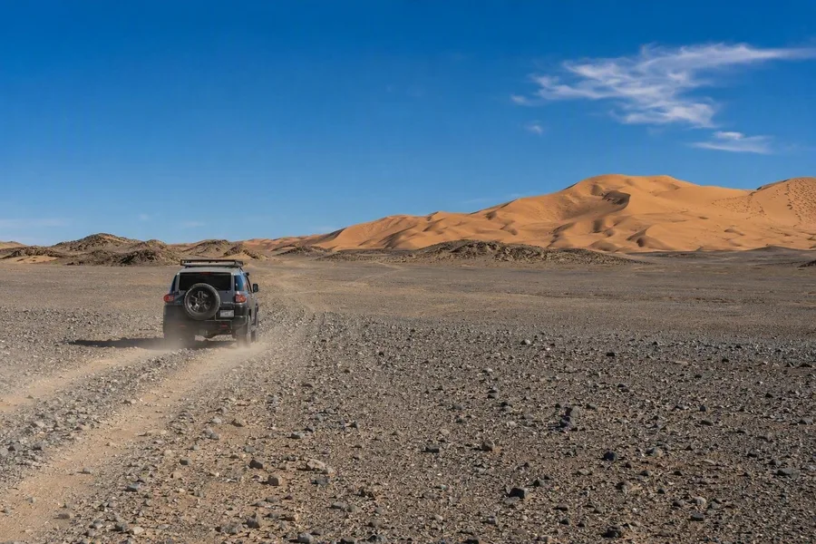 Een lokale chauffeur rijdt met een 4x4 over de grindvlakte van de Gobi naar Khongoryn Els.