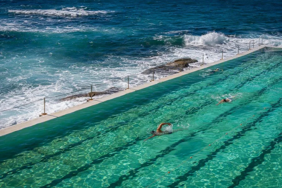 Zwemmers gebruiken de zoutwaterbanen van Bondi Icebergs naast de branding bij South Bondi.