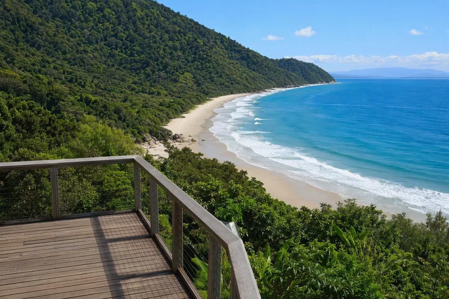 Het Kulki-uitkijkplatform kijkt uit over het zandstrand, de rotsige kapen en regenwoudhellingen van Cape Tribulation.