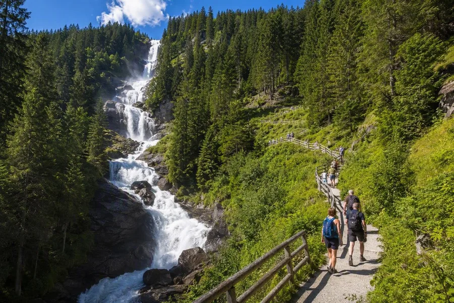 Bezoekers klimmen over het haarspeldpad langs de drie beboste trappen van de Krimmler Wasserfälle in Oostenrijk.