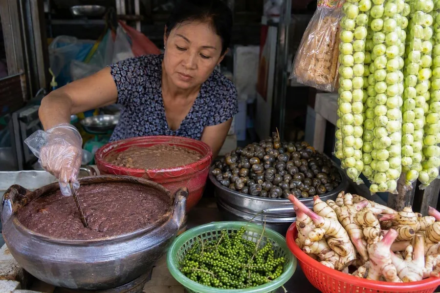 A vendor works beside fermented shrimp paste and river snails at Đông Ba Market in Huế.