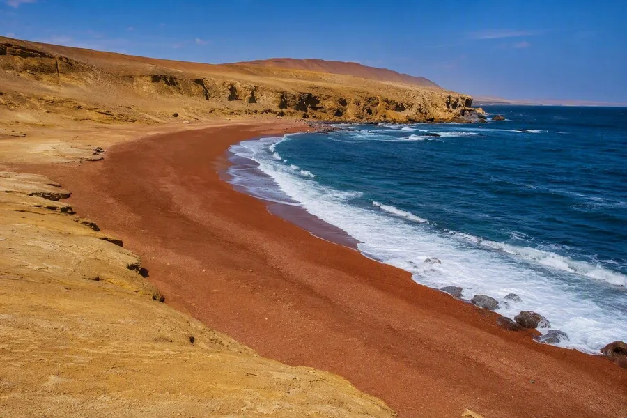 De roodbruine oever van Playa Roja buigt langs Peru’s koude Stille Oceaankust.