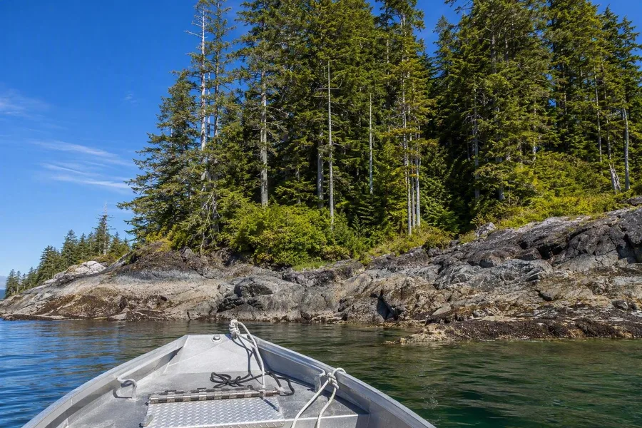 Een kleine boot nadert een rotsige kust van Gwaii Haanas onder cederbos.