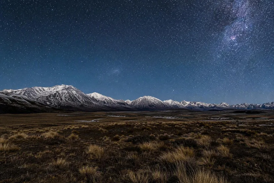 Sterren vullen de hemel boven pollen en donkere bergketens in het Mackenzie Basin.