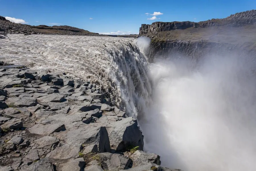 Grijsbruin water stort bij Dettifoss over een basaltlip in de kloof Jökulsárgljúfur.