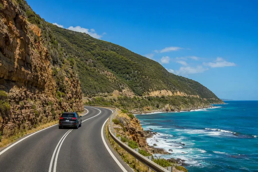 Een auto volgt de Great Ocean Road langs de rotswand tussen Eastern View en Apollo Bay.