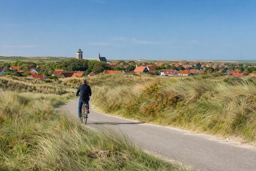 Een fietser volgt een duinroute op Schiermonnikoog, met het dorp in de verte.
