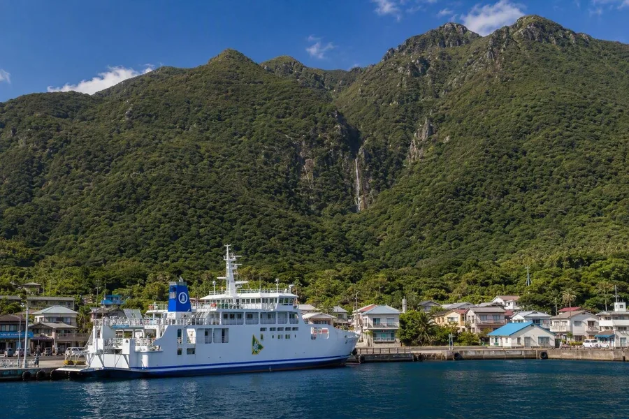 Een veerboot meert aan in Miyanoura, onder lage huizen en beboste hellingen.