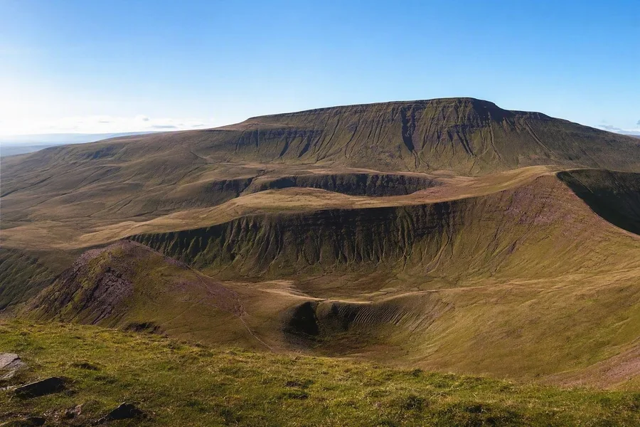 De brede zandstenen rug van Pen y Fan daalt af naar gletsjerdalen in Bannau Brycheiniog.
