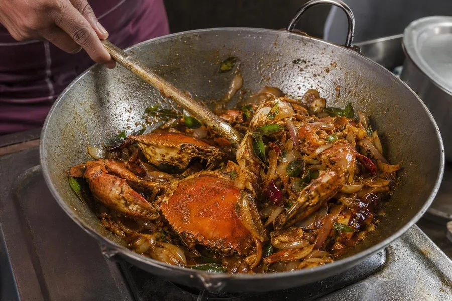 Een kok bakt hele modderkrab met specerijen voor Jaffnaanse krabcurry.