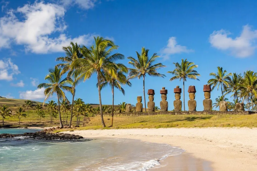 Gerestaureerde moai van Ahu Nau Nau staan achter het witte koraalzand van Anakena op Rapa Nui.