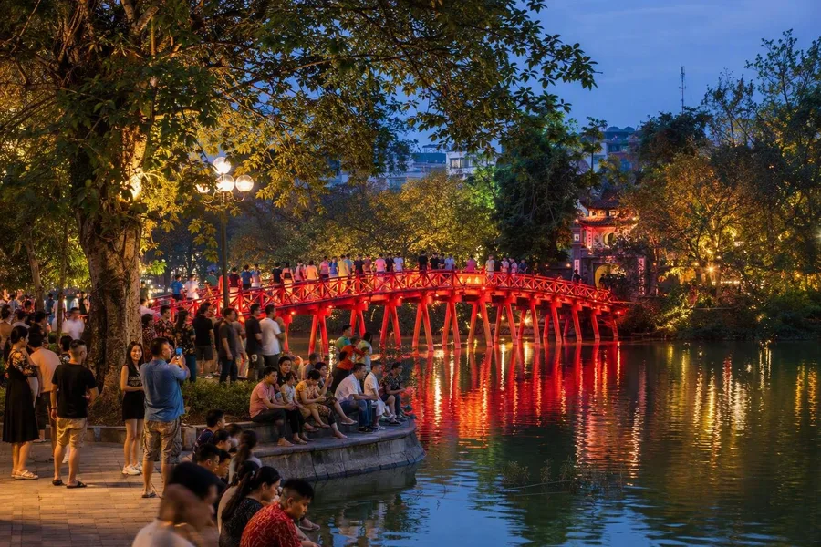 Families gather beside Hoàn Kiếm Lake as the red Húc Bridge leads to Ngọc Sơn Temple.